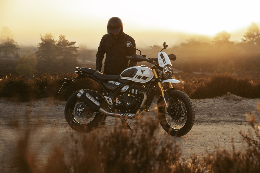 Triumph Unveils the All New 2026 Scrambler 400 XC 3 man standing behind a motorcycle parked on a dirt road