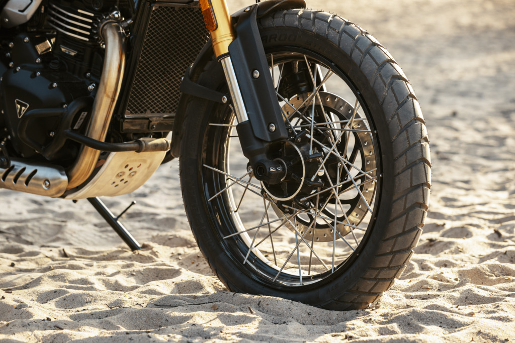 Triumph Unveils the All New 2026 Scrambler 400 XC 8 a close up view of a spoked rim and tire of a motorcycle parked in the sand