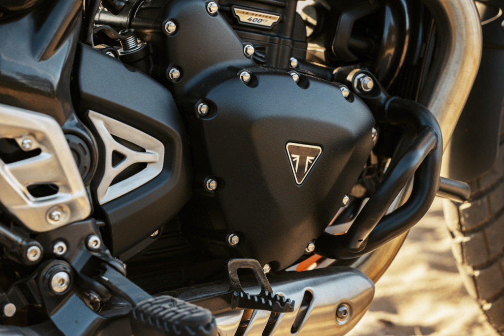Triumph Unveils the All New 2026 Scrambler 400 XC 12 a close up view of a gasket cover with the Triumph motorcycle emblem on it.