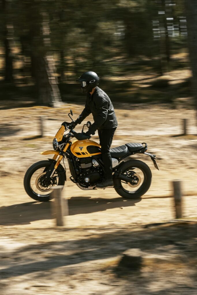 Triumph Unveils the All New 2026 Scrambler 400 XC 5 a man stands up riding a motorcycle on a dirt road