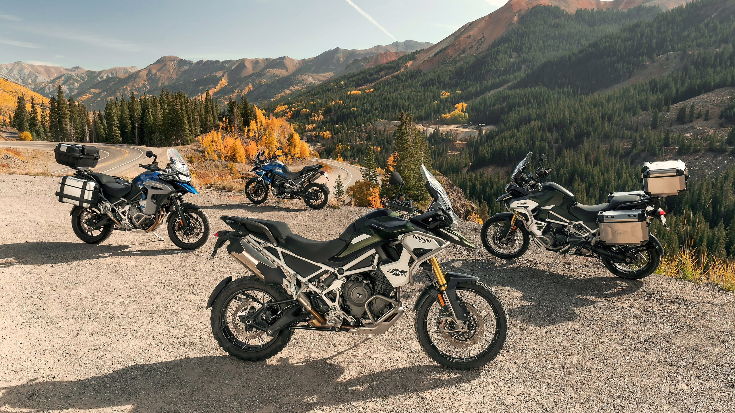 Four Triumph Tiger Adventure motorcycles parked on a dirt road.